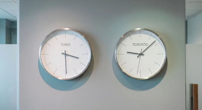Dual Timezone: A sleek, minimalist wall with two elegant analog clocks, one labeled "Tunis" and the other "Toronto," reflecting a clean, corporate aesthetic with soft green and blue shadows.